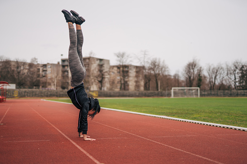 Young fitness woman doing handstand. On the running track.