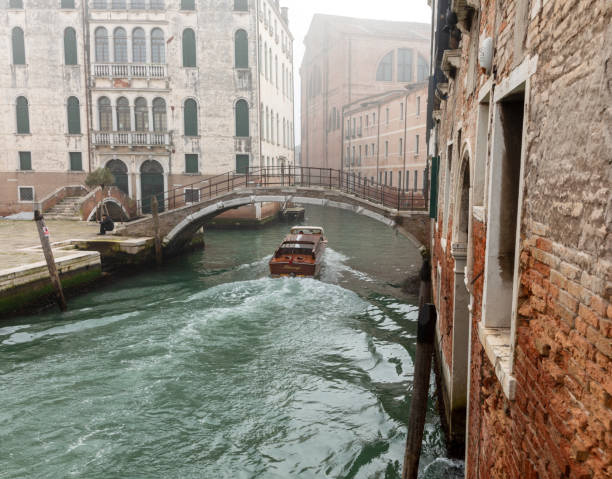 This is an image of a Venetian water taxi going under a bridge spanning one of the many canals in Venice