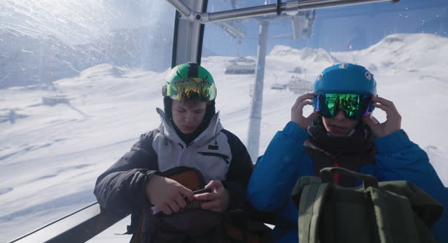 Two teenagers riding on gondola ski lift to the glacier ski slope in Austrian Alps.