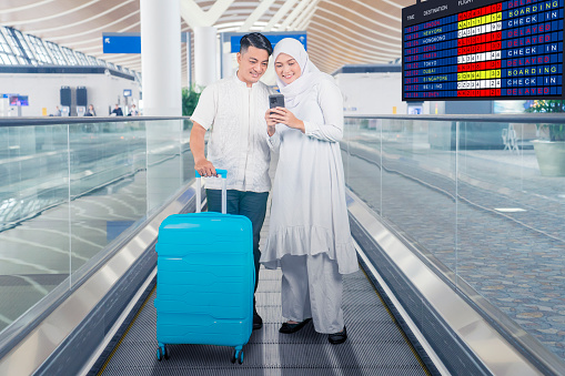 Muslim couple looking at a cellphone and standing with a suitcase on the airport moving walkways