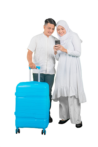 Muslim couple with a suitcase smiling looking at a mobile phone screen