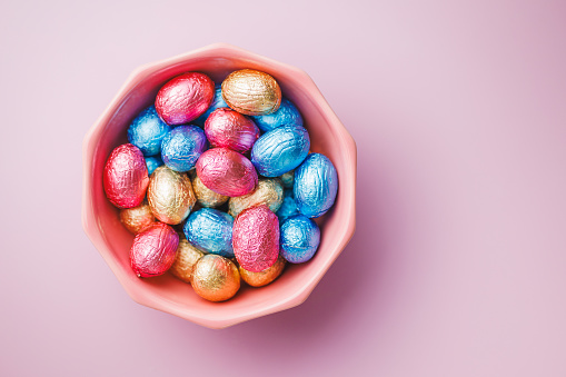 Easter chocolate eggs wrapped in aluminium foil in bowl on the pink background. Top view.
