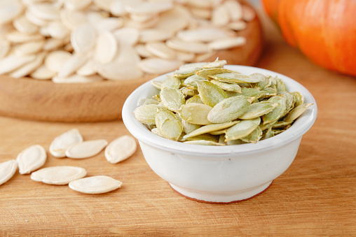 Peeled pumpkin seeds in a bowl on a wooden background. Front view from low angle. Close-up.