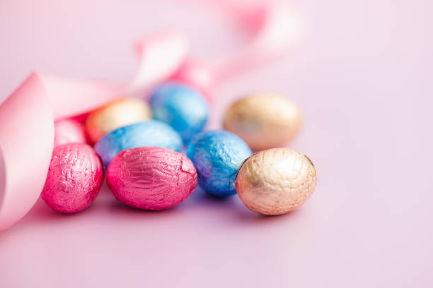 Easter chocolate eggs wrapped in aluminium foil on the pink background.