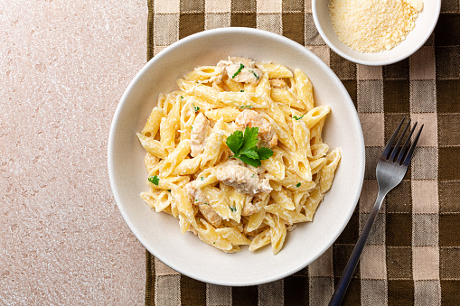 Chicken Alfredo penne, creamy pasta wich parmesan cheese in a white plate on a brown napkin. Directly above.