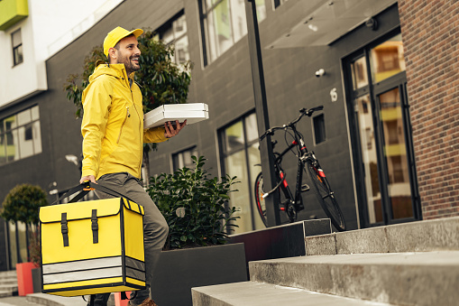 Young courier, pizza delivery man in uniform with thermo backpack on a bike. Home delivery.