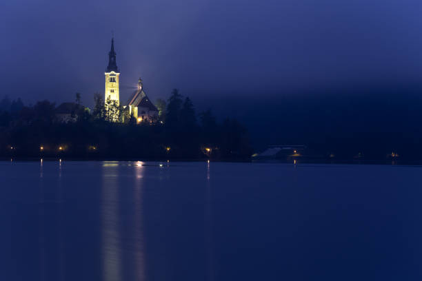 Early morning view to the Church on the Bled Lake. Reflection in the water. Long exposure, blurred clouds, smooth water. Slovenia Europe
