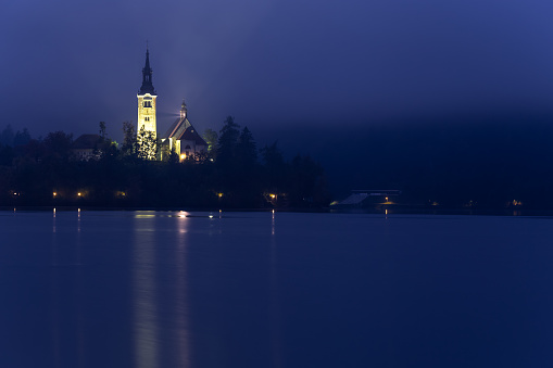 Early morning view to the Church on the Bled Lake. Reflection in the water. Long exposure, blurred clouds, smooth water. Slovenia Europe