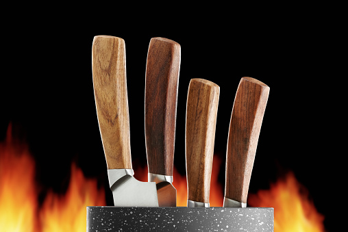 A set of kitchen knives in a stand on a background of flames of fire. Low angle view. Studio shot.
