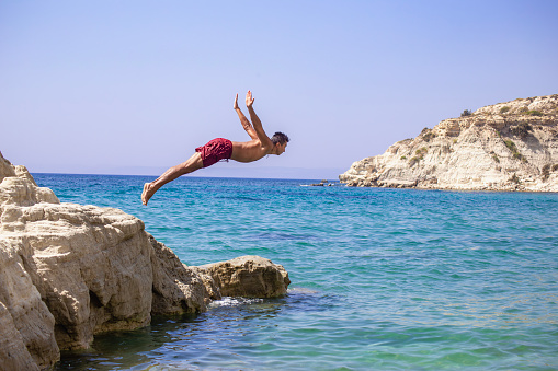 Young man jumping into the water from the cliff.