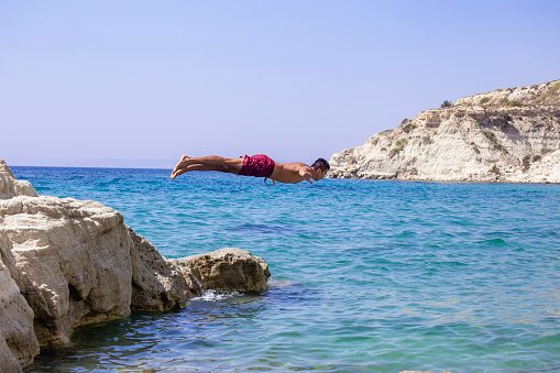 Young man jumping into the water from the cliff.