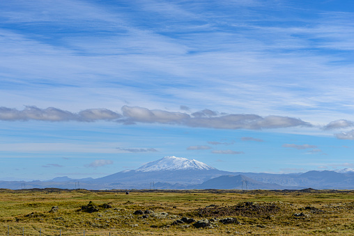 Panoramic view over the snowy mountains towards the Hekla volcano from the Markarfljót valley in Iceland during summer with soft hazy sunlight touching the mountains in the distance.