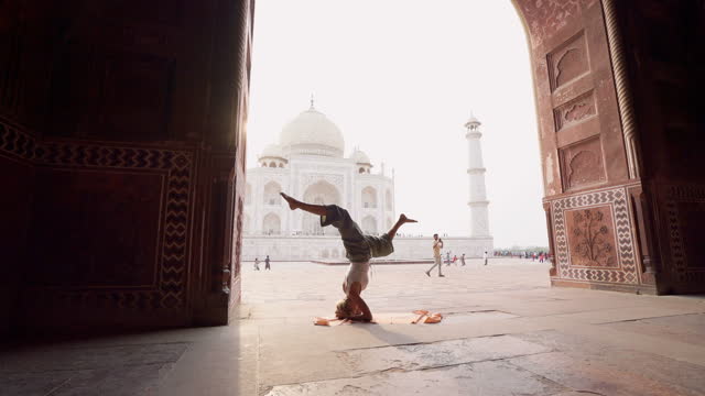 Young woman practicing yoga in India at the famous Taj Mahal at sunrise - Headstand position upside down- People travel spirituality zen like concept