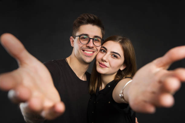 glückliches junges liebespaar, das selfie macht und lächelt, während es vor schwarzem hintergrund steht. - adult isolated color image studio shot stock-fotos und bilder