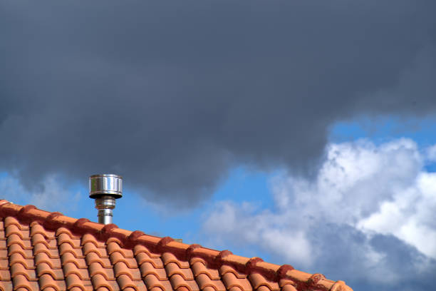Steel chimney cap on a roof against cloudy sky