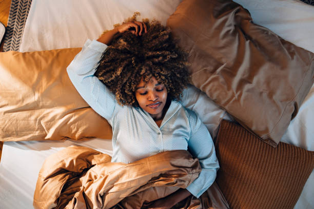 Relaxed Young Woman Lying in Bed with Eyes Closed in Cozy Environment Overhead view of a peaceful young woman lying comfortably in bed with closed eyes, exuding calmness and tranquility indoors. hair on pillow stock pictures, royalty-free photos & images