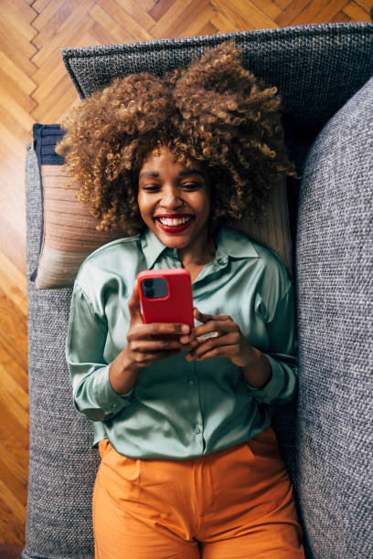 Joyful Woman Relaxing on a Couch Using Her Smartphone at Home