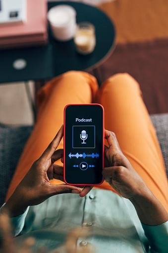 Over-the-shoulder view of a woman checking a podcast app on her smartphone, cozy at home setting.