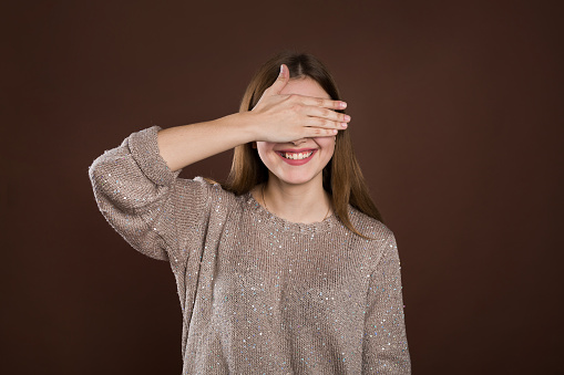 smiley woman covering her eyes by hands over brown background
