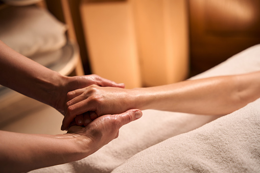 Cropped photo of masseuse stretching thumb and little finger of female client