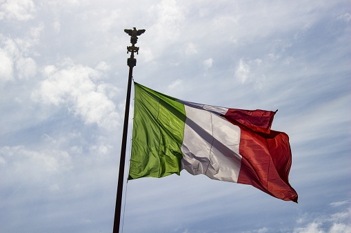 The Italian flag waving in the clear sky as a symbol of independence, spreading light and peace around.