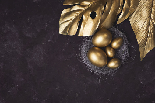 Golden monstera leaf and eggs in nest on dark black background. A background for celebrating Easter Top view and copy space Flatlay. Luxury background and Minimal black
