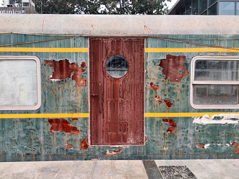 The side of an abandoned, blue train car with a rusted panel