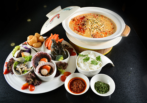 spicy mala laksa curry hot clay pot with seafood prawn, scallop, chicken meat, vegetable, noodle and chilli sambal thick gravy sauce in bowl on black table asian halal food cuisine menu for restaurant