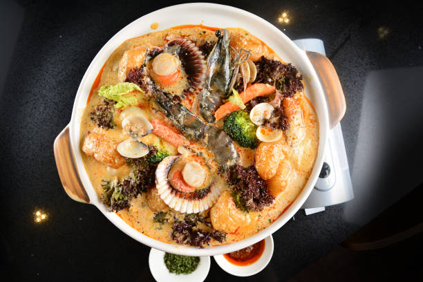 spicy mala laksa curry hot clay pot with seafood prawn, scallop, chicken meat, vegetable, noodle and chilli sambal thick gravy sauce in bowl on black table asian halal food cuisine menu for restaurant
