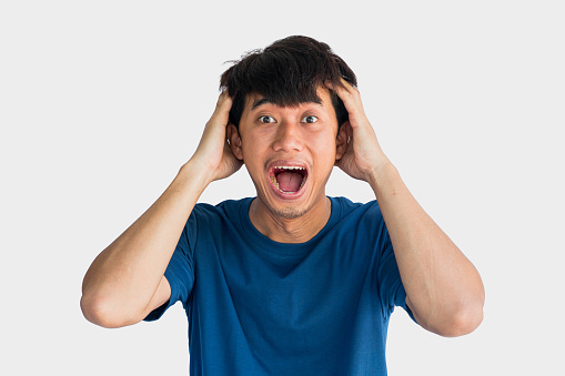 Young Asian man in blue t-shirt having a big surprise, isolated on gray background. The concept of the arrival of big luck.