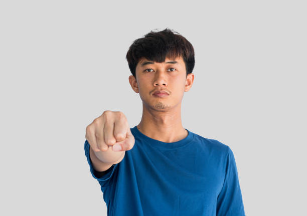 ritratto di un giovane asiatico felice che indossa una maglietta blu che stringe un pugno davanti a lui, isolato su uno sfondo grigio. - signal box foto e immagini stock