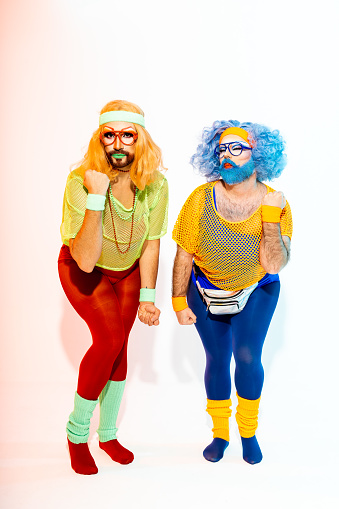 Two drag queens in colorful 80s attire, complete with leggings and headbands, strike a playful pose.