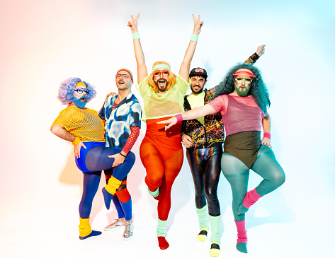 Full body of drag queens in colorful body fit sportswear and costumes standing together in various feminine style in studio with white background