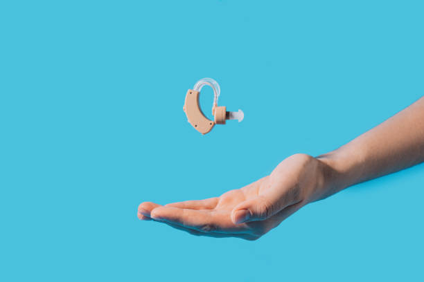 Hearing aid hovering above the hand against a blue background.