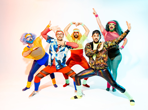 A vibrant group of colorful drag queens and queer friends strikes superhero poses in retro attire, embodying confidence and flamboyance.