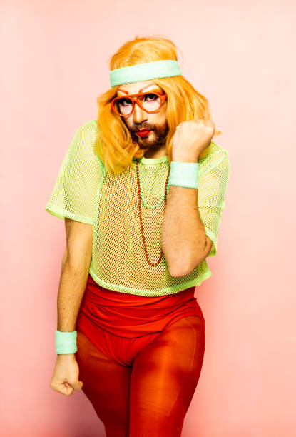 Drag queen in a vintage 80s-style outfit, with a headband and glasses, strikes a playful pose while engaging in a workout routine.