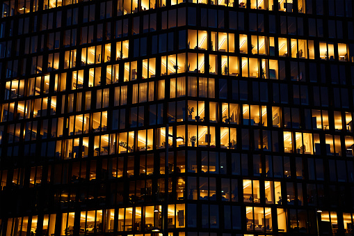 Office building lights up the evening with windows glowing in the dusk, showcasing urban work life after hours