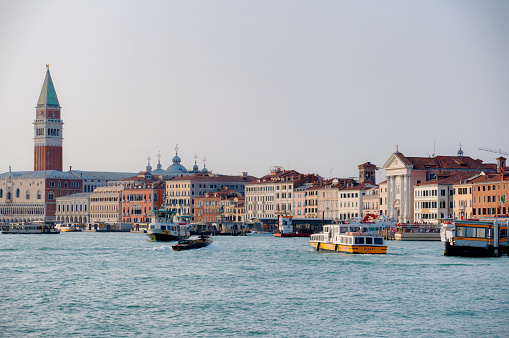 Venice, Italy - February 20, 2022: Vaporettos and speedboats ply the bustling waters of the Grand Canal in Venice, with the towering form of St Mark's Campanile in the background.