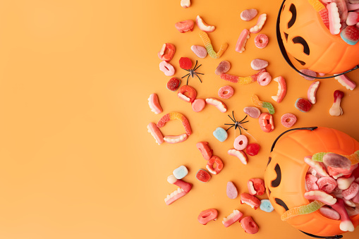 Baskets in the form of pumpkins with sweets and spiders on an orange background.