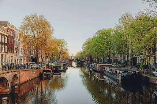 Canal lined with brick row houses on a sunny summer day. A bicycle chained to a bridge railing is in foreground. The Hague, Netherlands.