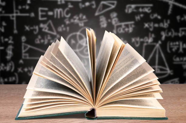 istock Open Textbook on Desk Against Blurred Blackboard With Mathematical Equations 2040076993
