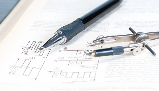 The pencil and circlet are on an open page of a technical reference book with electrical diagrams close up