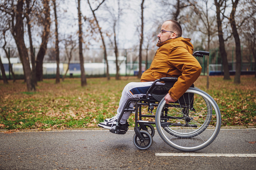 Portrait of paraplegic handicapped man in wheelchair in park. He is rolling on pathway.