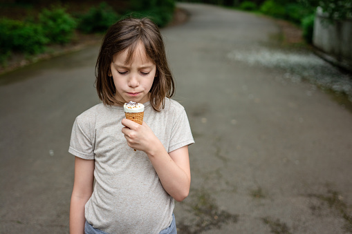 Girl holding ice cream in the park during summer day.