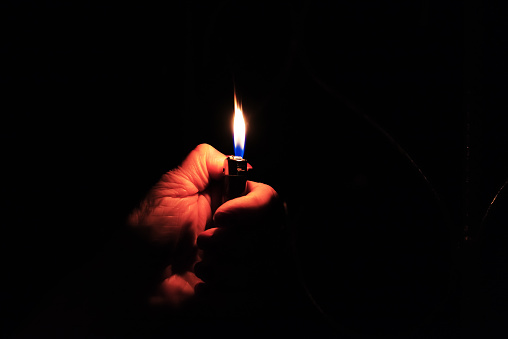 Woman hand holding a burning lighter in the dark black background.Closeup,selective focus.Copy space.