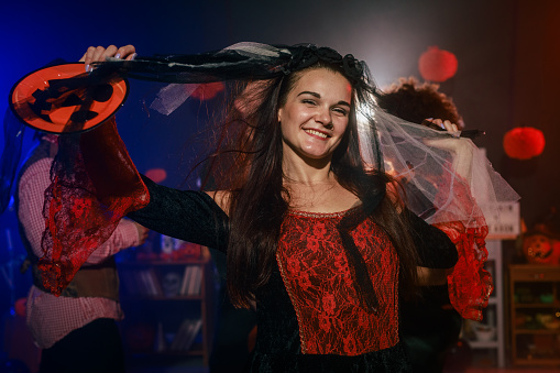 Portrait of charming young woman dancing in costume during a fun Halloween party with friends. She is looking at camera, smiling joyfully with confidence.