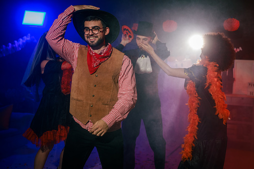 Portrait of cheerful young man in a cowboy costume dancing during a Halloween party with friends.