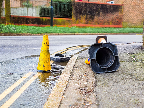 A drain overflows with water at the side of the road, due to excessive rainfall.