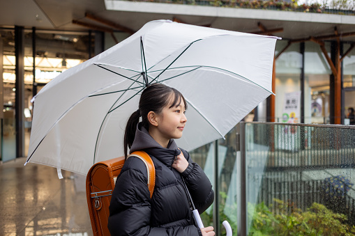 Japanese elementary school student girl carrying a ‘randoseru’ school bag in a rainy day
