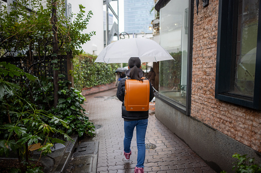 Rear view of Japanese elementary school student girl carrying a ‘randoseru’ school bag in a rainy day